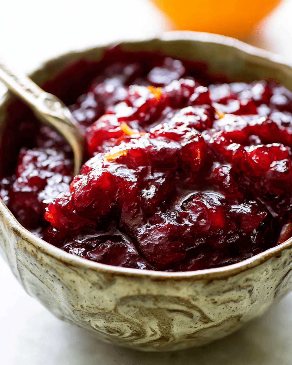 A rustic bowl filled with vibrant homemade cranberry sauce, with a spoon partially dipped in.
