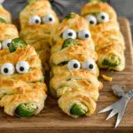 Jalapeno Popper Mummies made with puff pastry and candy eyes arranged on a wooden board.