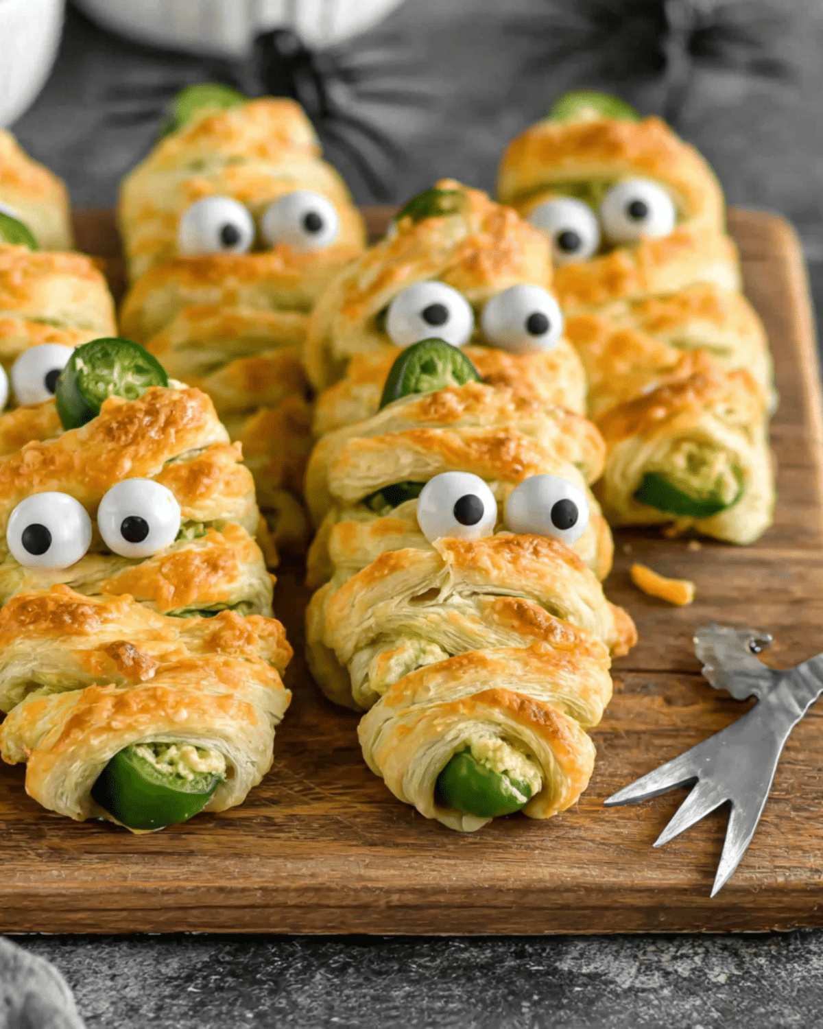 Jalapeno Popper Mummies made with puff pastry and candy eyes arranged on a wooden board.