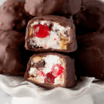 Close-up of Martha Washington Candy filled with cherries, coconut, and pecans, coated in chocolate and stacked on a white pedestal plate.
