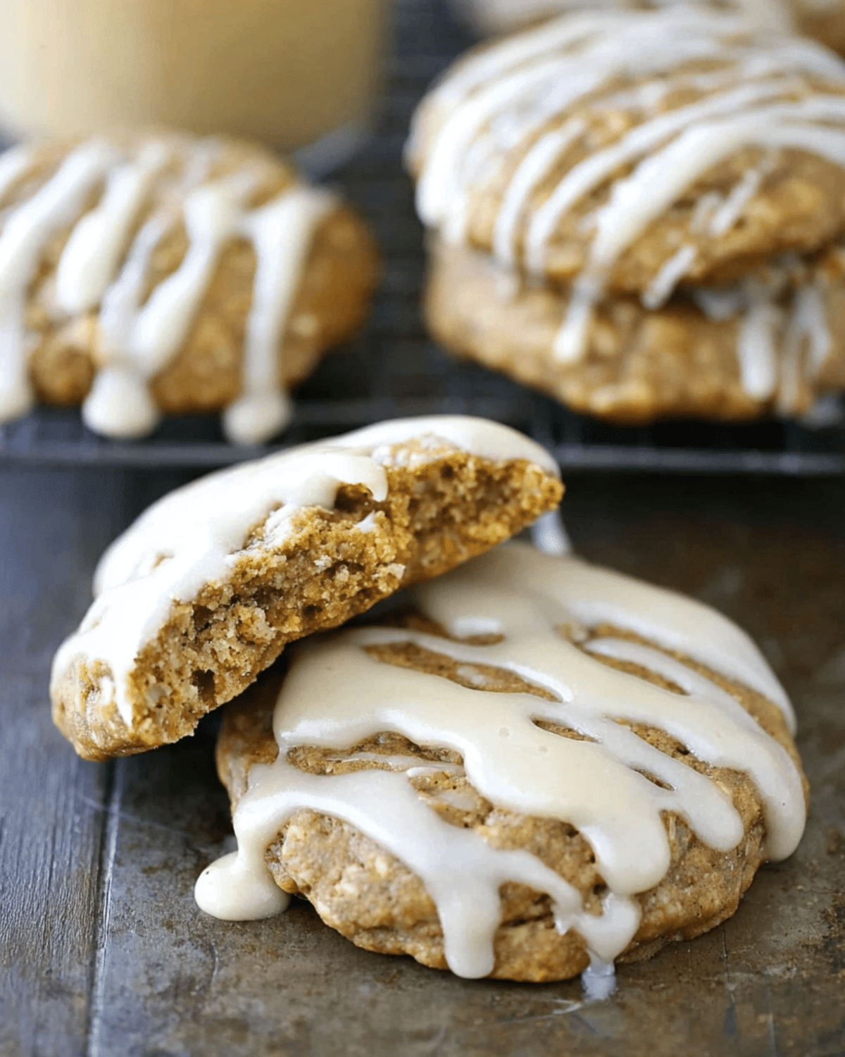 Soft Maple Pumpkin Cookies topped with a drizzle of icing, with one cookie broken in half to show the moist interior.