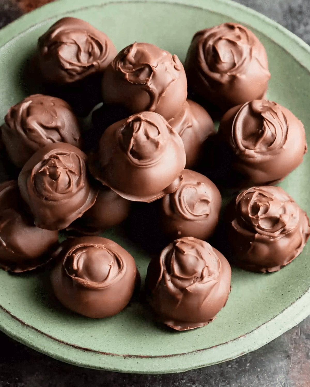 A green plate filled with No Bake Chocolate Chip Cookie Dough Truffles coated in smooth chocolate.