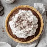 A no-bake chocolate pudding pie topped with whipped cream and chocolate shavings, set in a graham cracker crust.