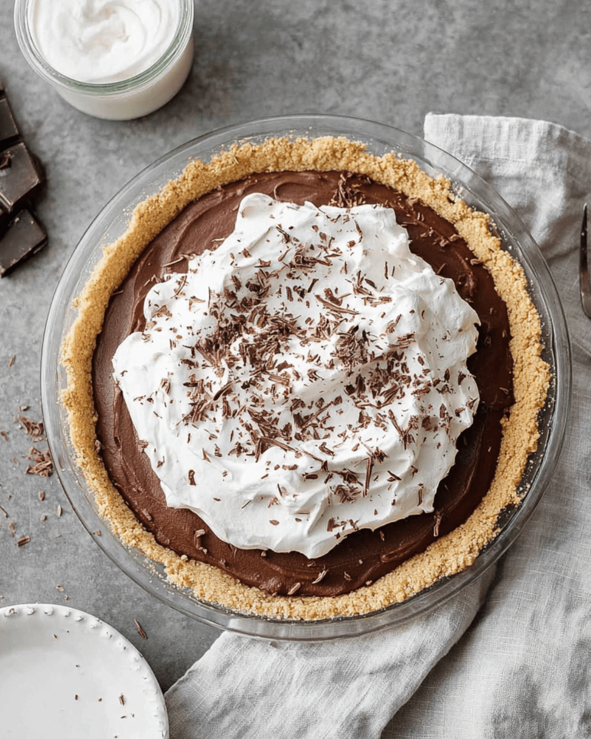A no-bake chocolate pudding pie topped with whipped cream and chocolate shavings, set in a graham cracker crust.