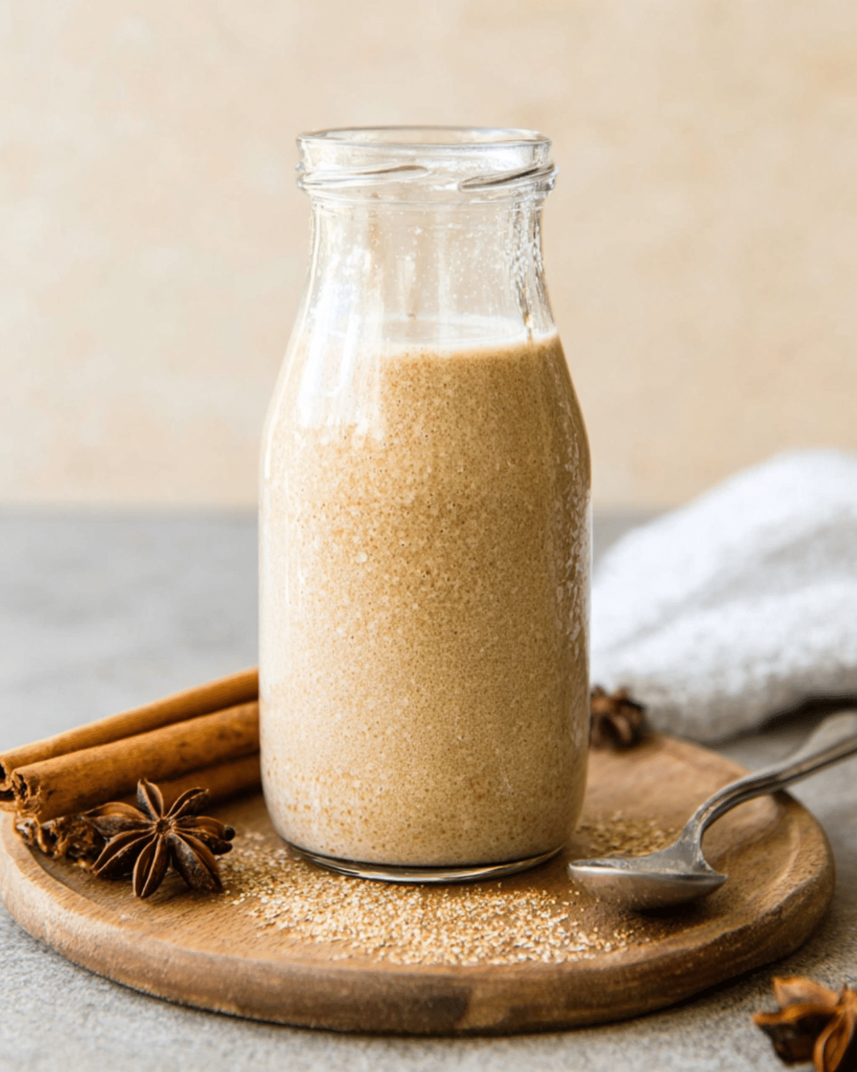 A glass bottle filled with homemade Oatmilk Pumpkin Spice Creamer, placed on a wooden board with cinnamon sticks and star anise.