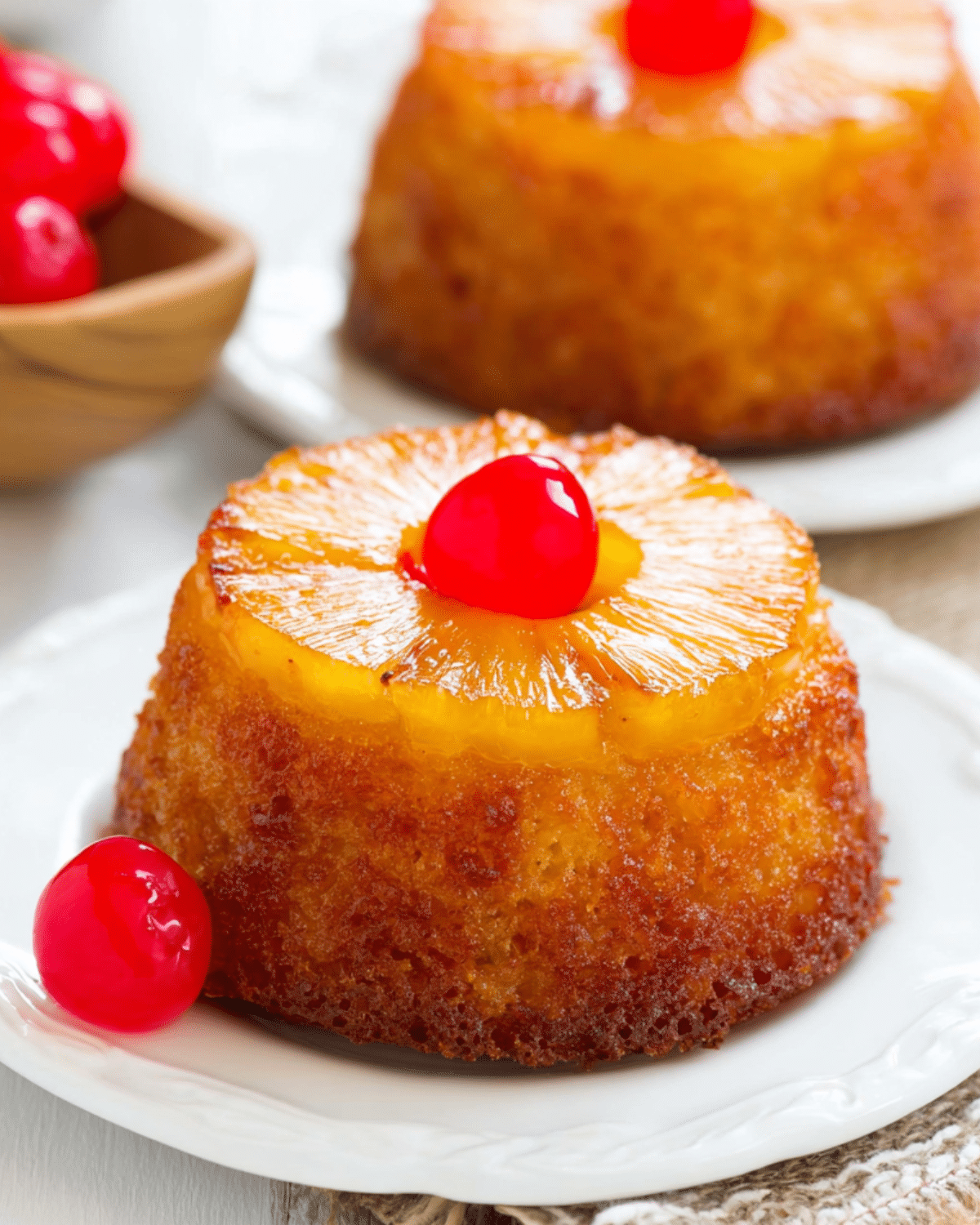 Pineapple Upside Down Mini Cakes topped with a pineapple ring and a bright red cherry on a white plate.