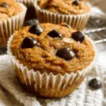 Close-up of Pumpkin Protein Muffins topped with chocolate chips, resting on a white cloth.