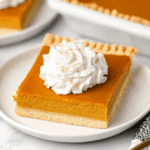 A square slice of Pumpkin Slab Pie topped with whipped cream and a sprinkle of cinnamon on a white plate.