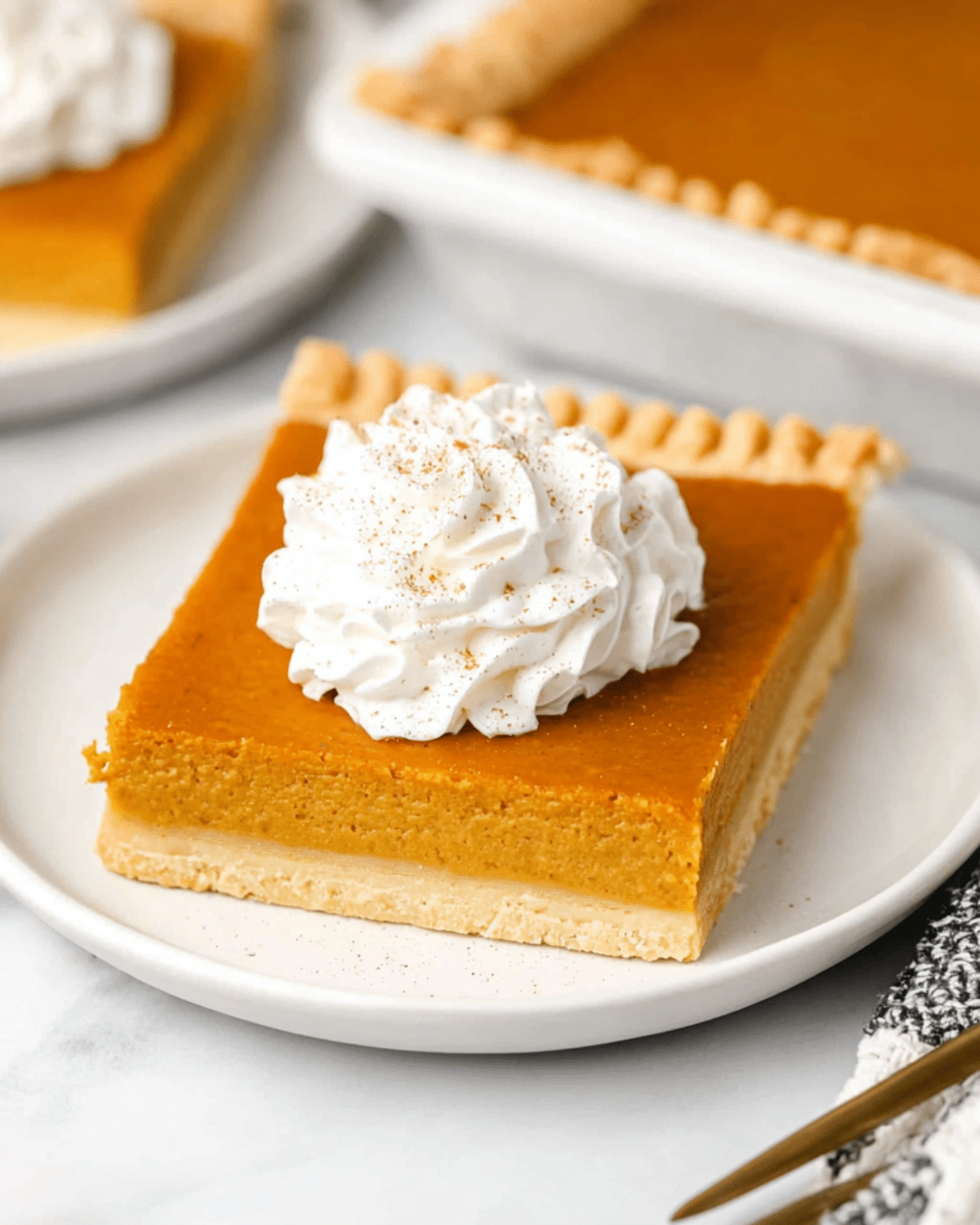 A square slice of Pumpkin Slab Pie topped with whipped cream and a sprinkle of cinnamon on a white plate.