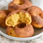 Plate of pumpkin sourdough bagels, with one split open to show its soft, spiced interior and cinnamon-sugar coating.