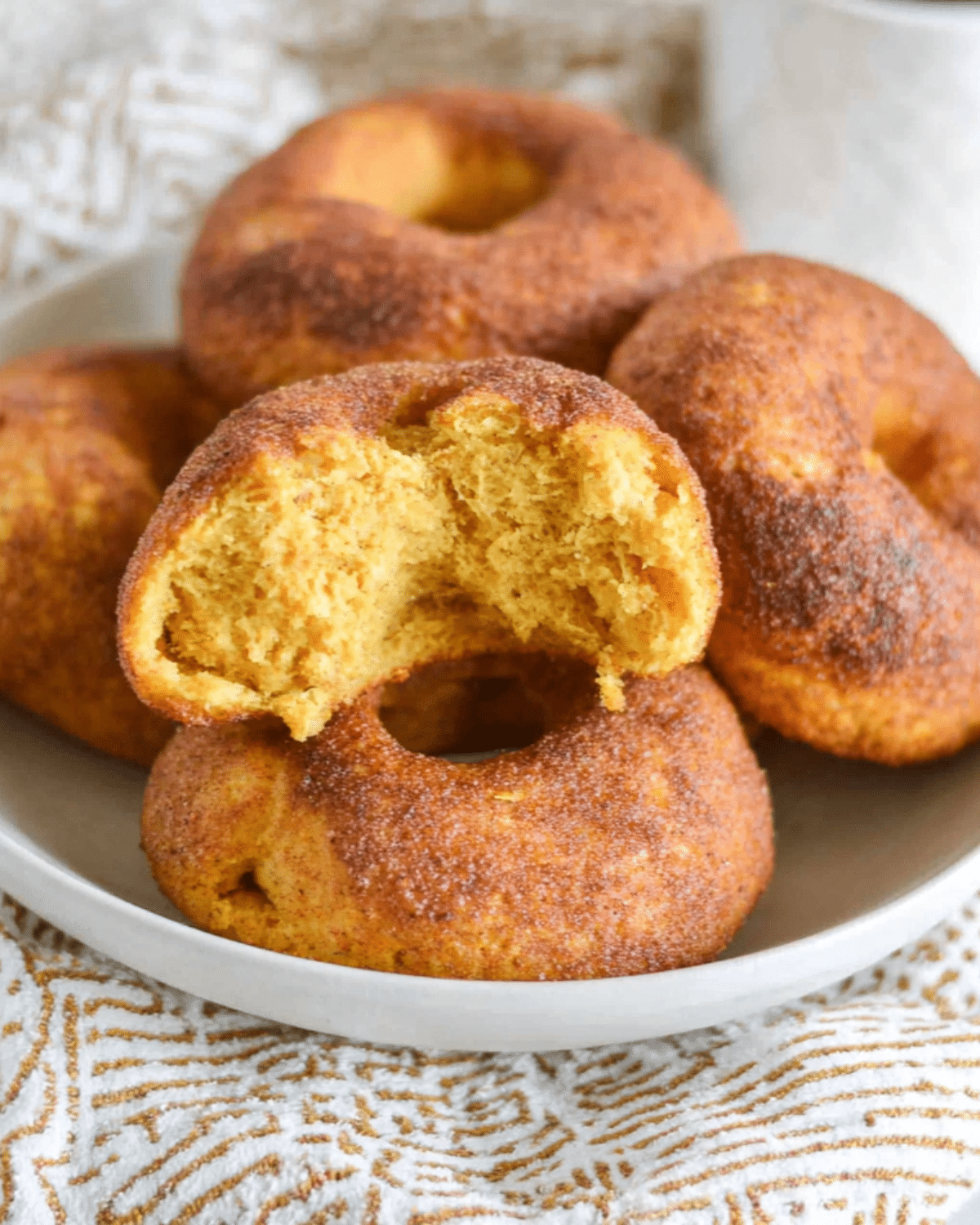 Plate of pumpkin sourdough bagels, with one split open to show its soft, spiced interior and cinnamon-sugar coating.