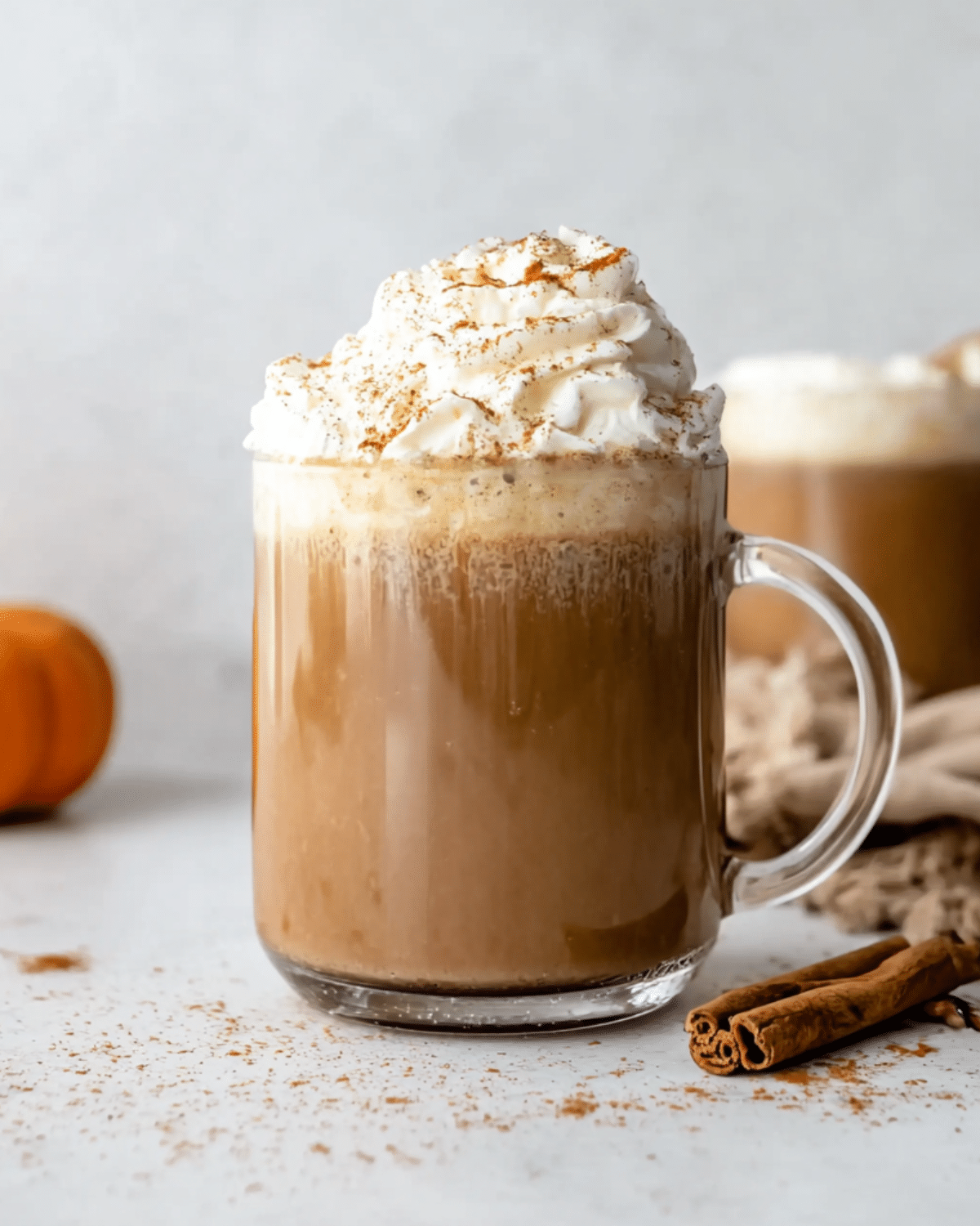 Glass mug filled with a pumpkin spice latte topped with whipped cream and sprinkled with cinnamon.