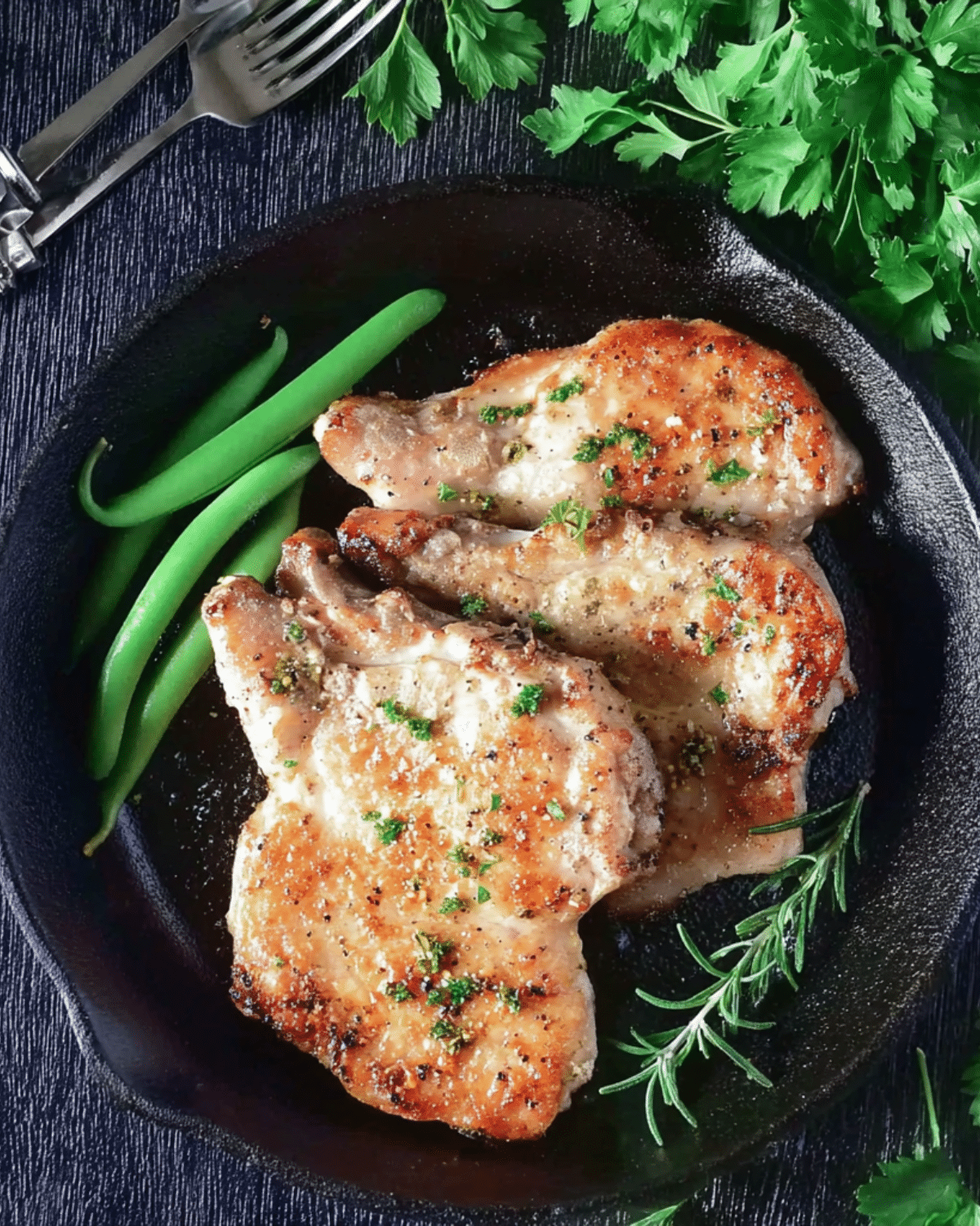 Skillet of ranch pork chops garnished with herbs, served with fresh green beans and rosemary.