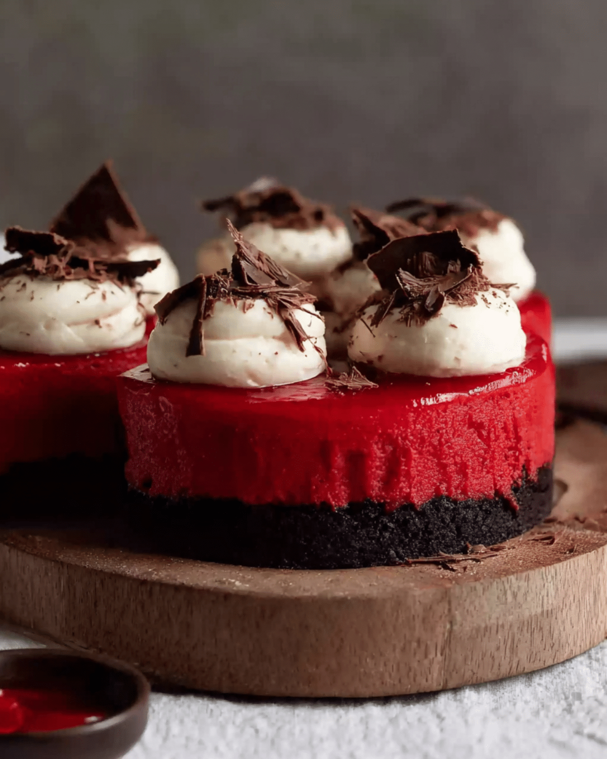 Mini Red Velvet Cheesecakes with a chocolate cookie crust, topped with cream cheese frosting and chocolate shavings.