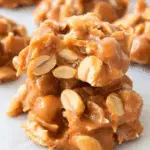 Close-up of Salted Peanut Caramel Clusters stacked on parchment paper, packed with peanuts and gooey caramel.