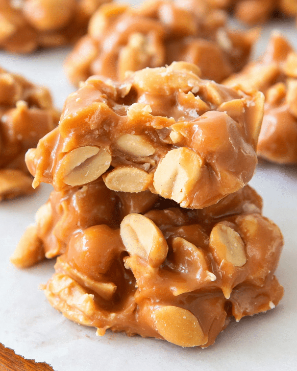 Close-up of Salted Peanut Caramel Clusters stacked on parchment paper, packed with peanuts and gooey caramel.