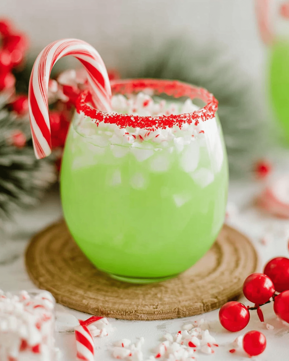 A festive glass of The Grinch Punch with a red sugar rim, crushed peppermint, and a candy cane garnish.
