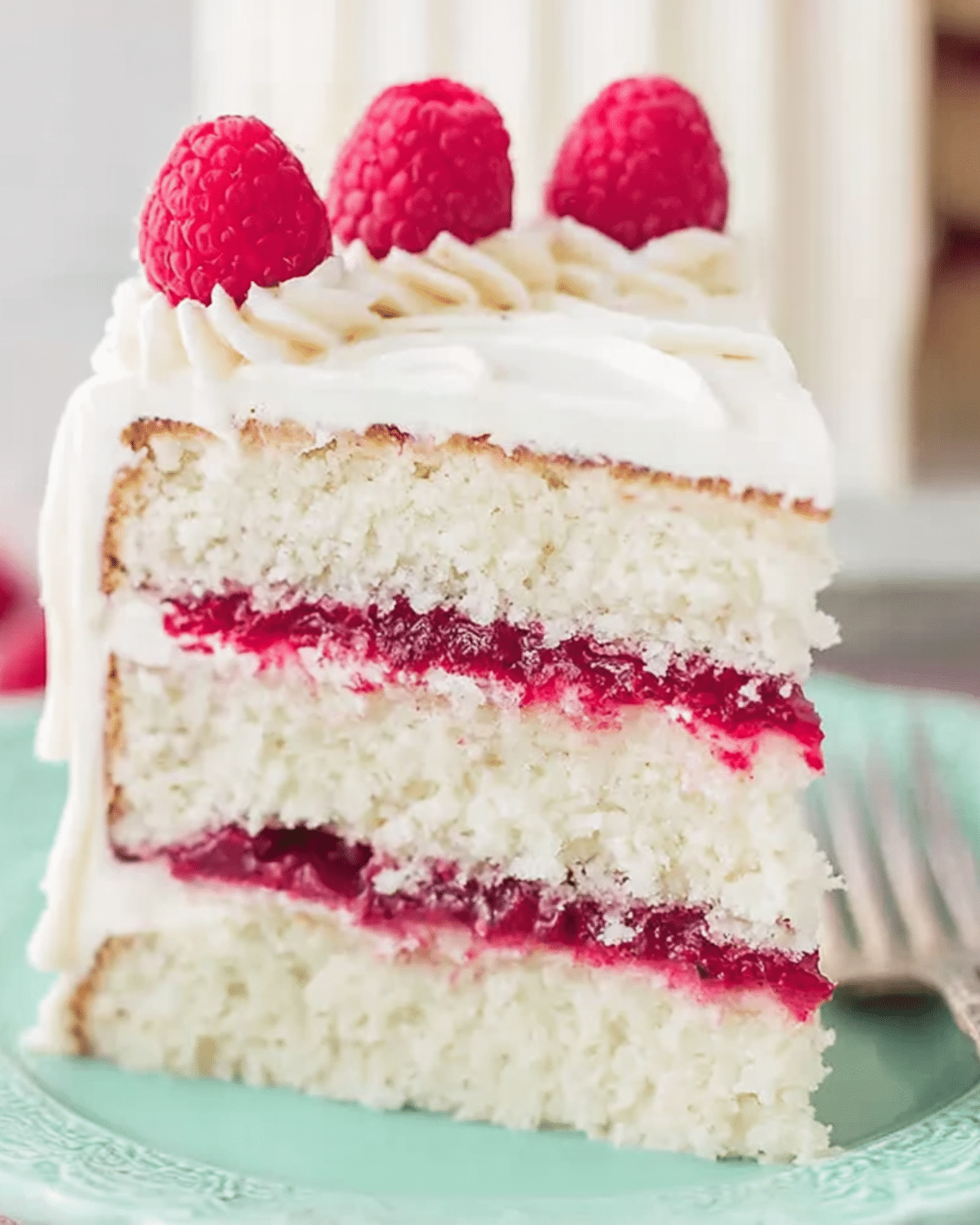 Slice of white chocolate raspberry cake with raspberry filling and fresh raspberries on top.