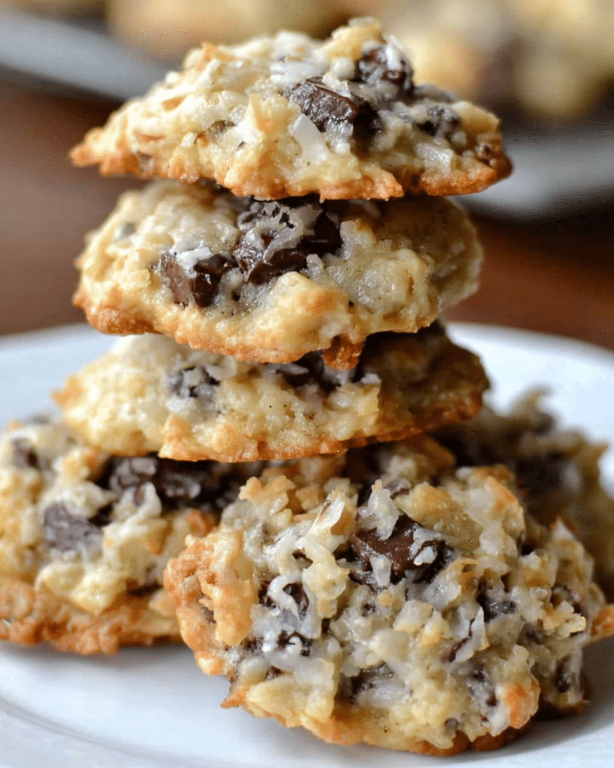 Stack of Almond Joy cookies filled with shredded coconut, chocolate chunks, and almonds on a white plate.