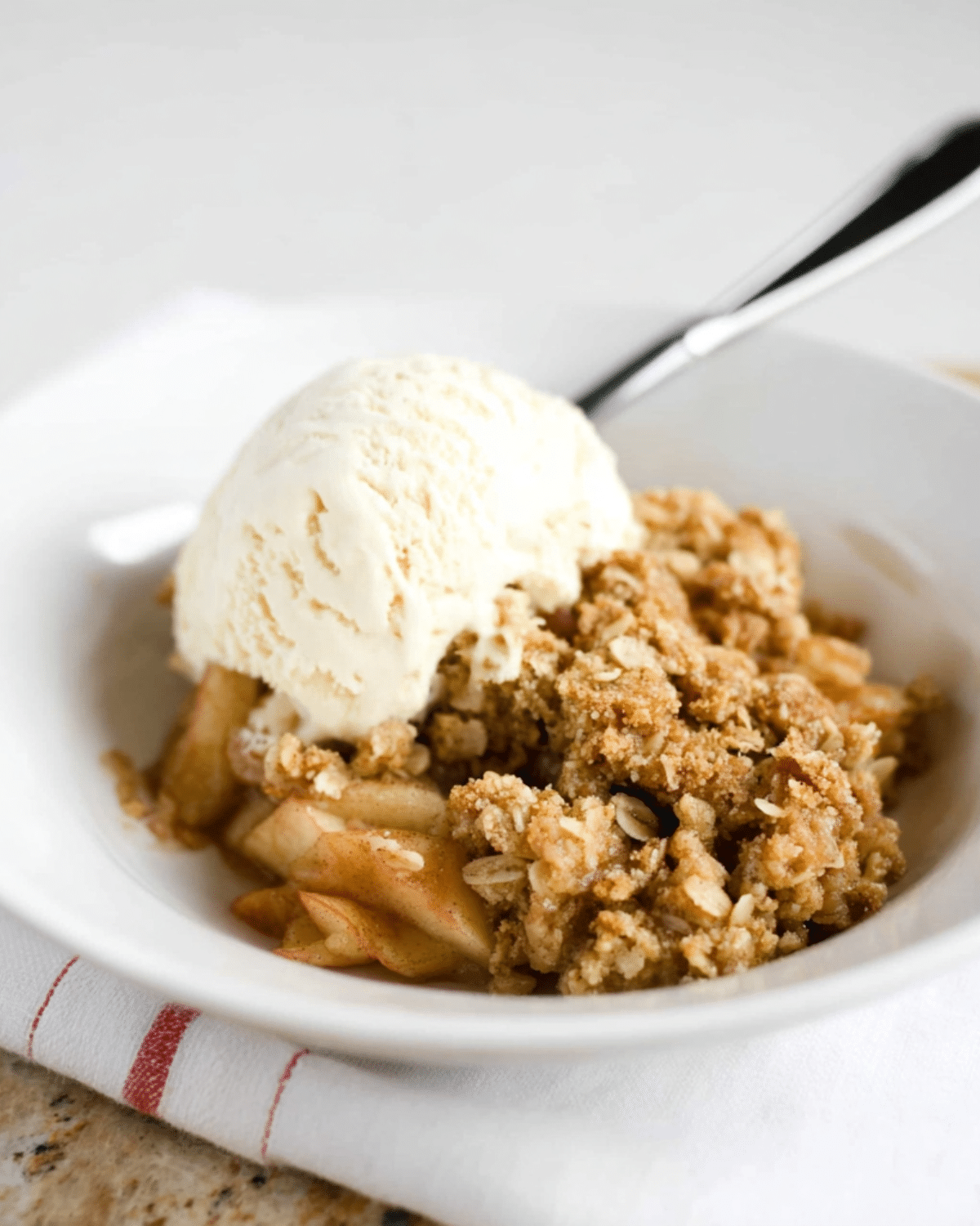 Bowl of brown sugar apple oat crisp topped with vanilla ice cream, showcasing tender apple slices and a golden oat crumble.