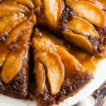 Caramel apple upside-down cake with glossy caramelized apple slices arranged on top, and a slice being served from the whole cake.