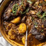 Tender Cider Braised Pot Roast with golden crispy sage potatoes in a rustic Dutch oven, garnished with fresh herbs.