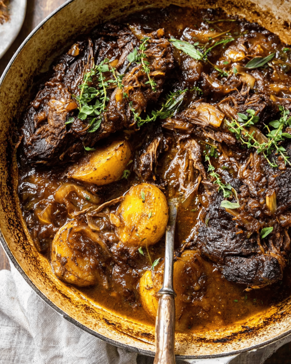 Tender Cider Braised Pot Roast with golden crispy sage potatoes in a rustic Dutch oven, garnished with fresh herbs.