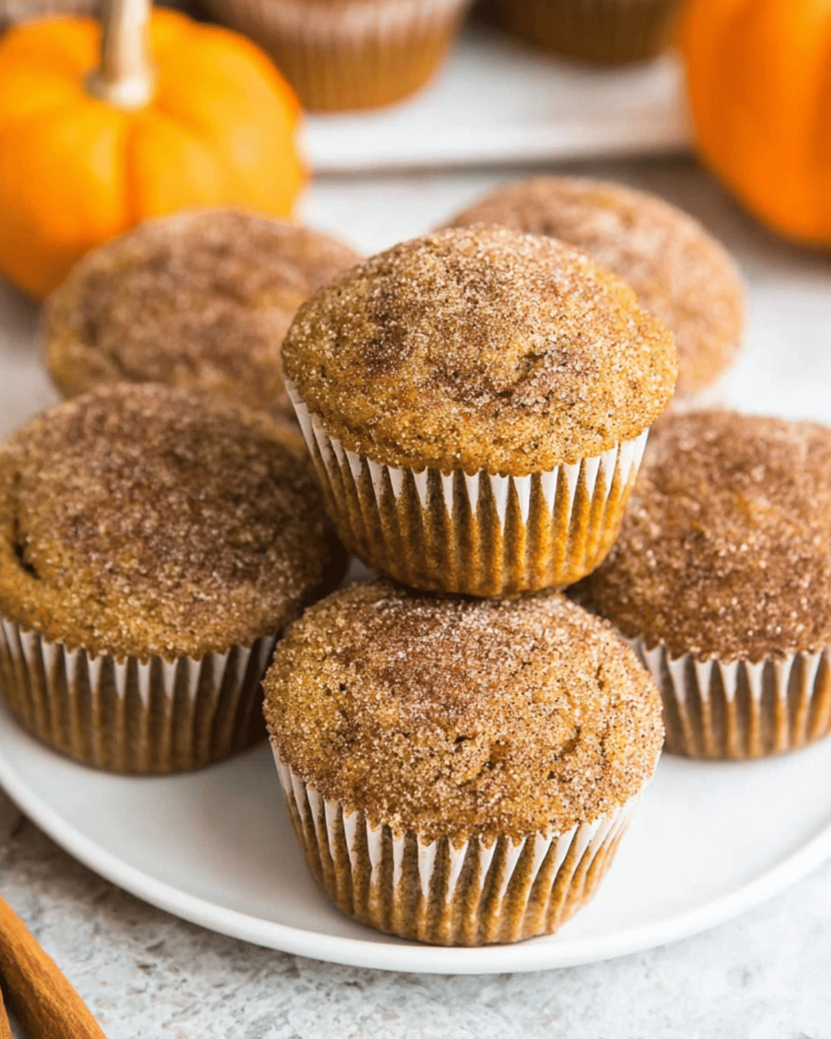 Cinnamon Sugar Pumpkin Muffins stacked on a white plate with mini pumpkins in the background.