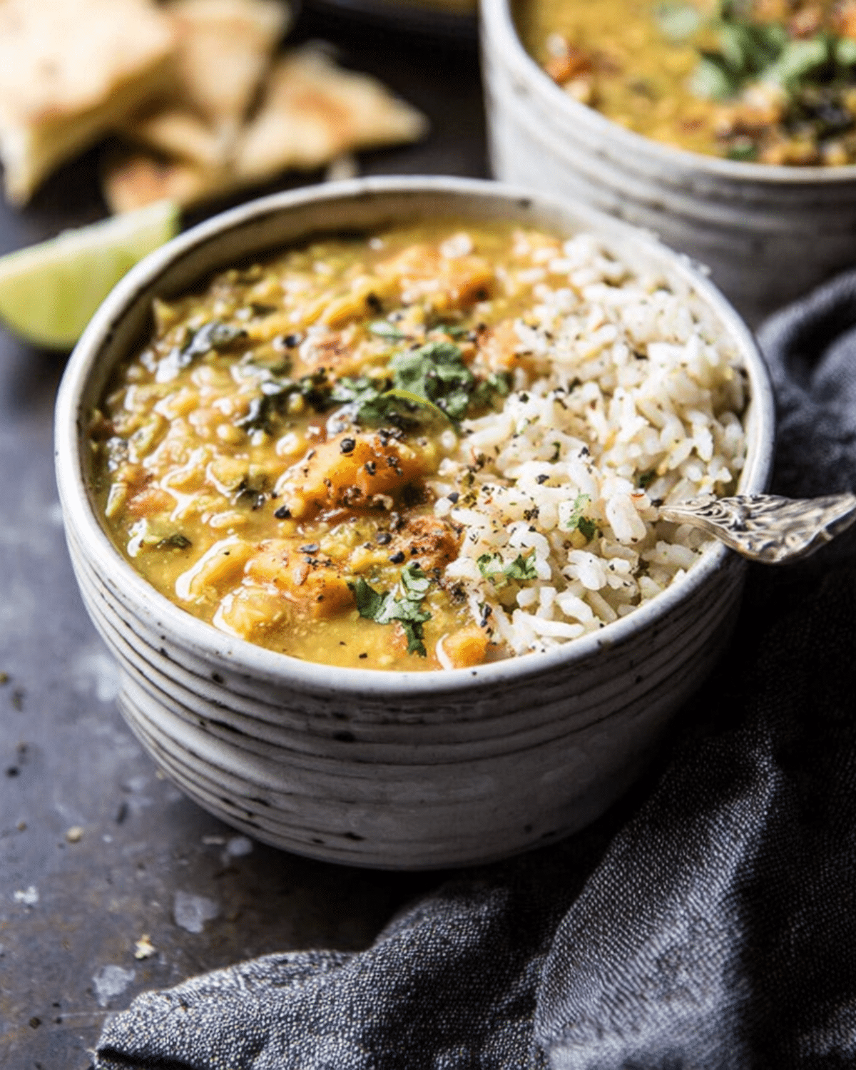 A bowl of coconut sweet potato lentil soup served with a scoop of white rice, garnished with fresh cilantro and cracked black pepper.