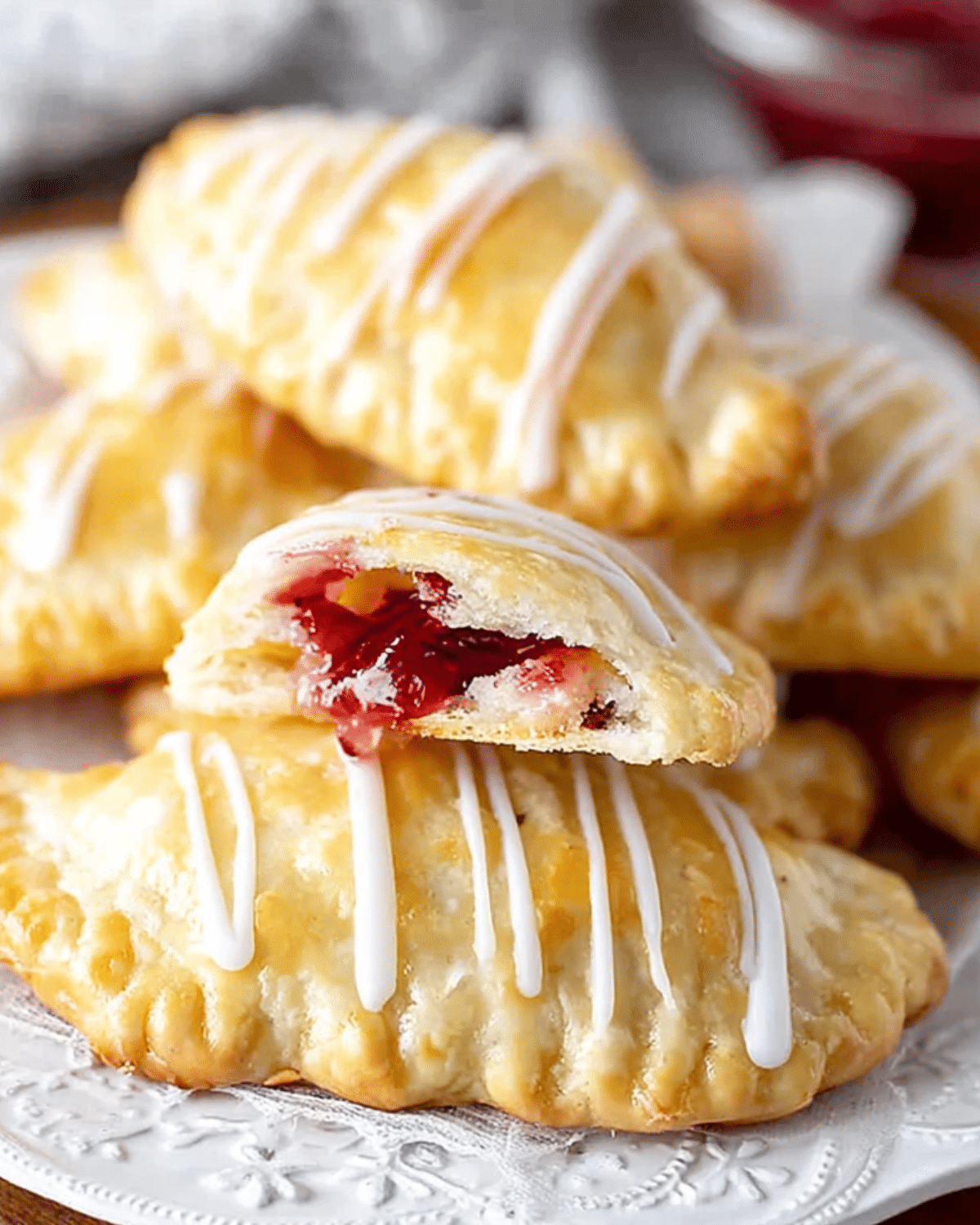 Golden-brown cookie empanadas filled with red fruit jam, drizzled with white icing and stacked on a decorative plate.