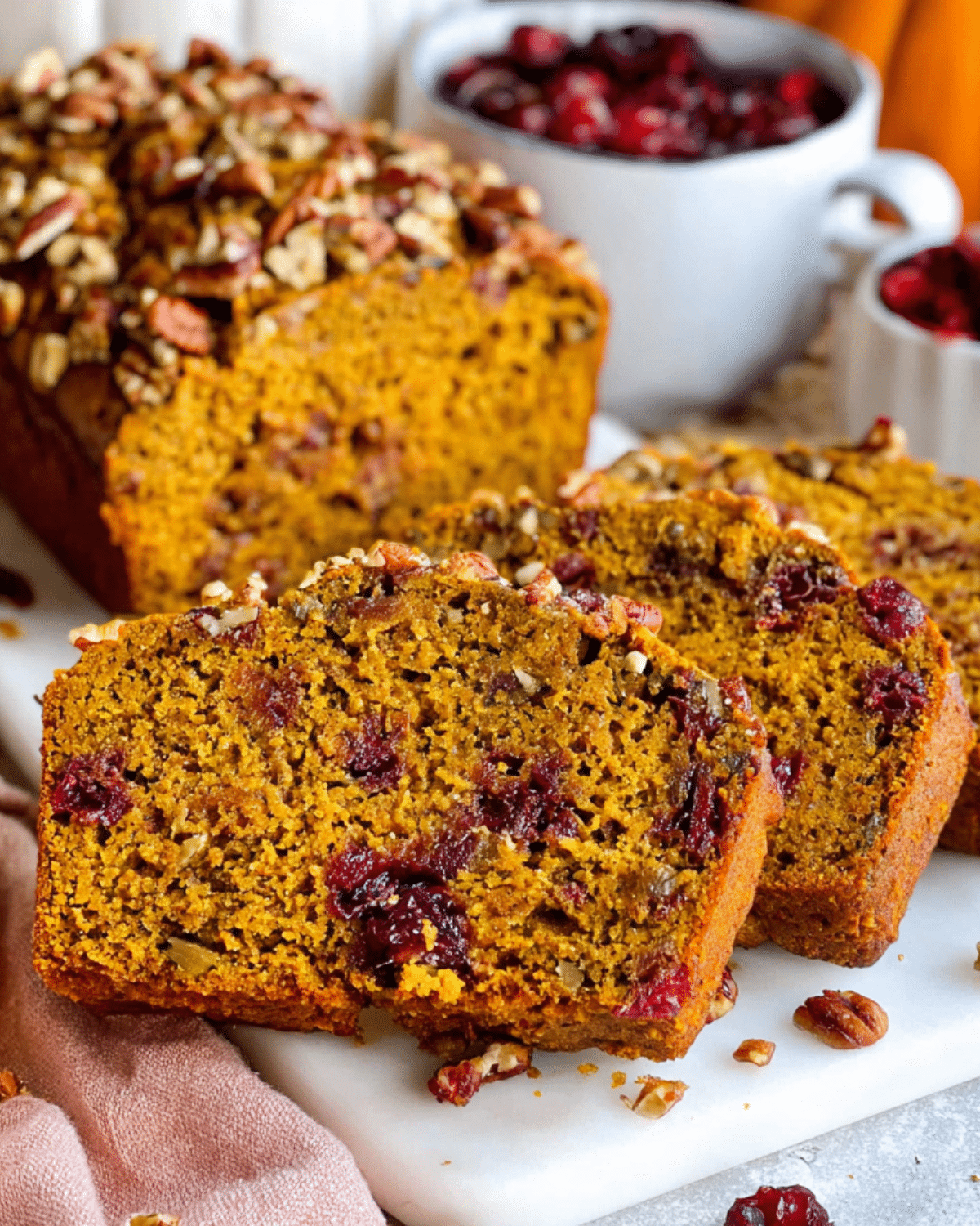 Sliced cranberry pecan pumpkin bread topped with chopped pecans, with visible cranberries inside the moist loaf.
