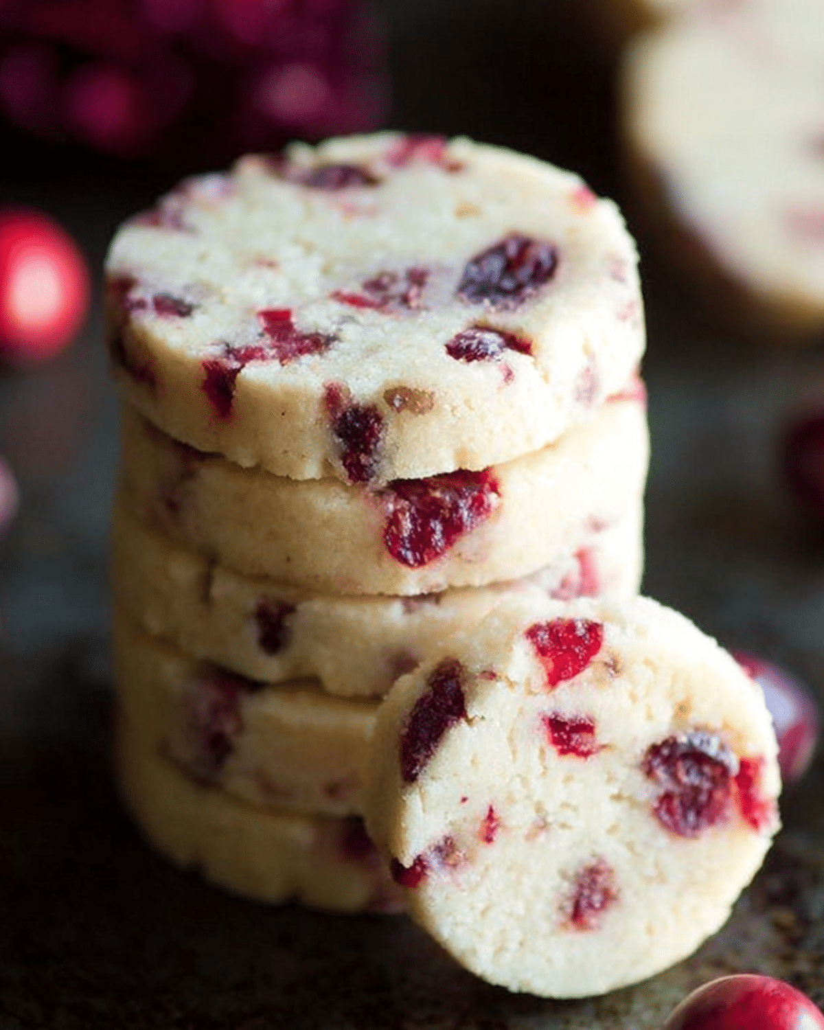 Stack of Cranberry Shortbread Cookies with bits of dried cranberries throughout, displayed on a dark surface.