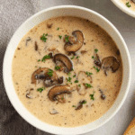 A bowl of creamy mushroom soup topped with fresh parsley and sliced sautéed mushrooms.