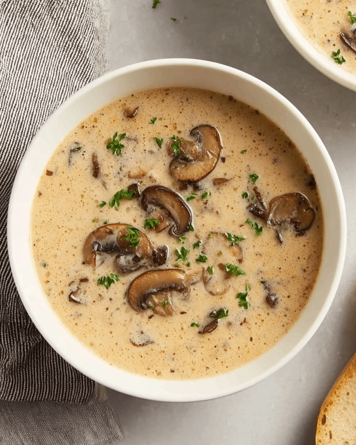 A bowl of creamy mushroom soup topped with fresh parsley and sliced sautéed mushrooms.