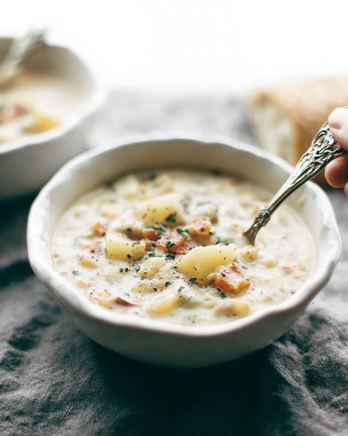 A bowl of creamy potato soup with chunks of potato, carrots, and herbs, being stirred with a spoon.