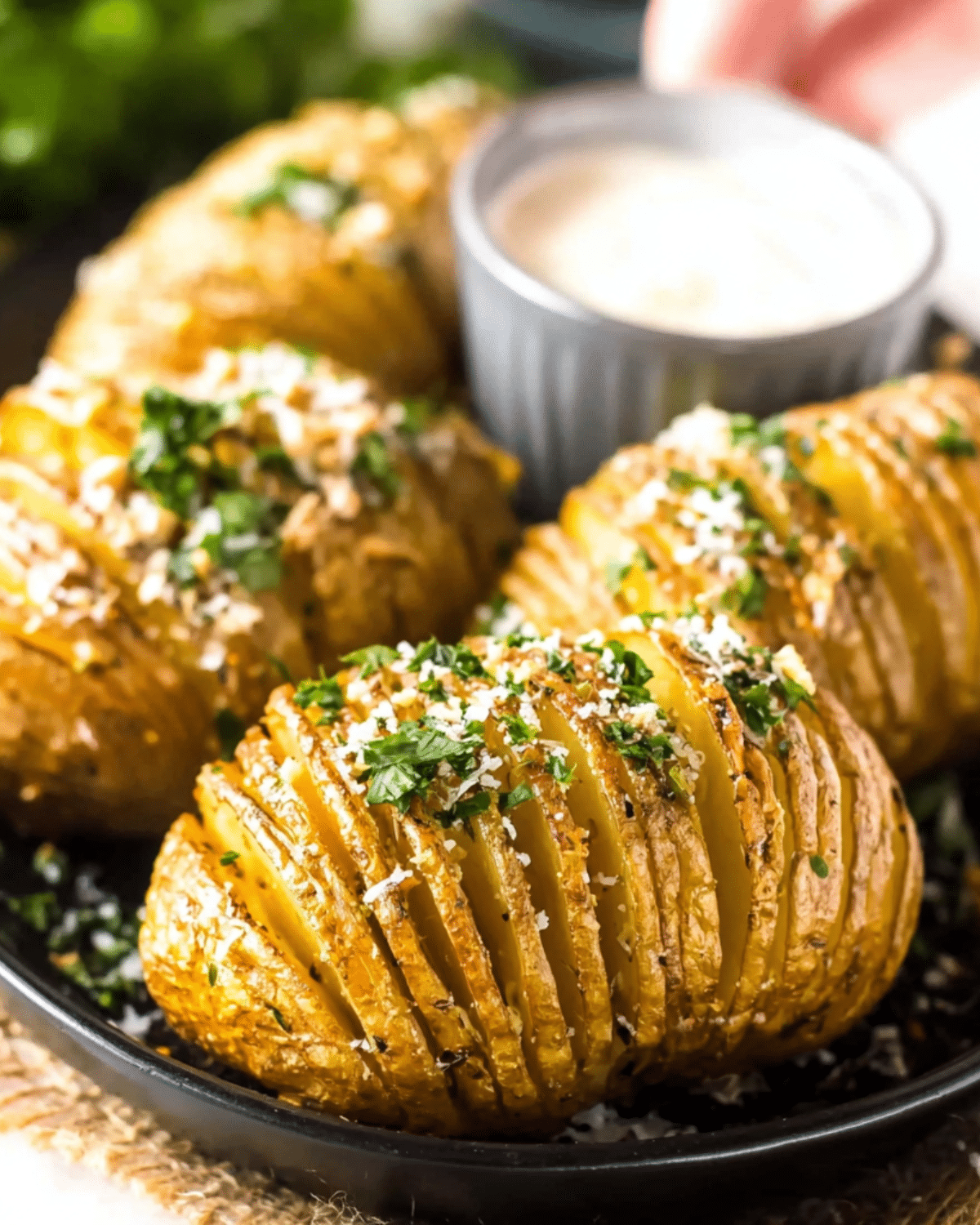 Crispy Hasselback potatoes garnished with herbs and Parmesan, served with a creamy dipping sauce.