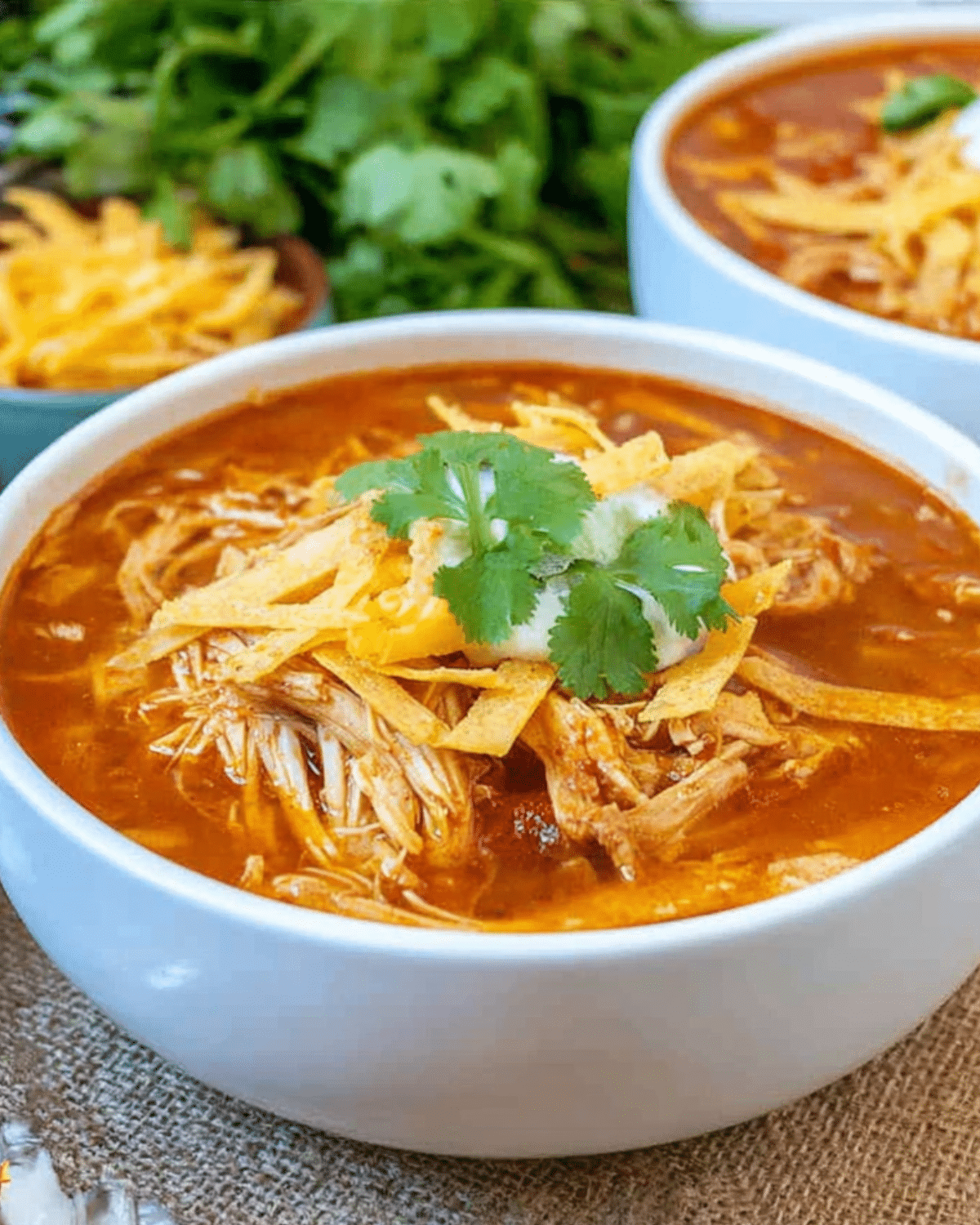 A white bowl filled with Crockpot chicken tortilla soup, topped with shredded cheese, tortilla strips, sour cream, and fresh cilantro.