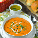 Easy creamy tomato soup in a white bowl, garnished with a swirl of cream and chopped herbs, served with fresh bread and olive oil on the side.