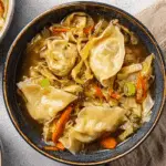 A bowl of easy potsticker soup filled with dumplings, shredded cabbage, carrots, and green onions.
