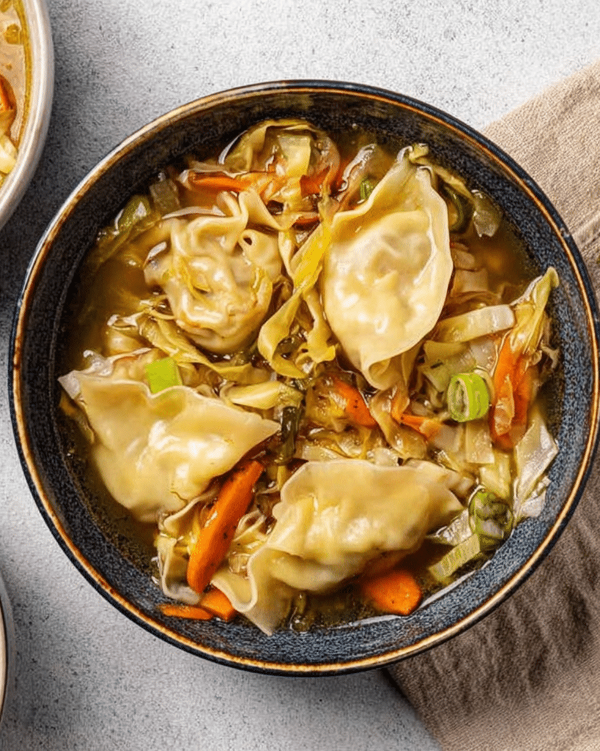 A bowl of easy potsticker soup filled with dumplings, shredded cabbage, carrots, and green onions.