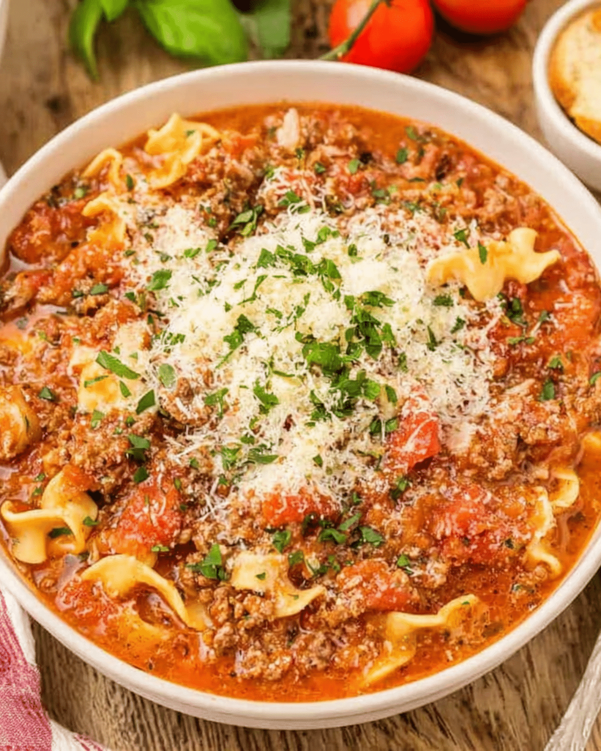 A bowl of hearty Italian lasagna soup filled with ground meat, tomato chunks, lasagna noodles, and topped with grated Parmesan and fresh parsley.