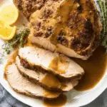 Juicy slow cooker turkey breast sliced and topped with rich brown gravy, served with lemon slices and fresh herbs.