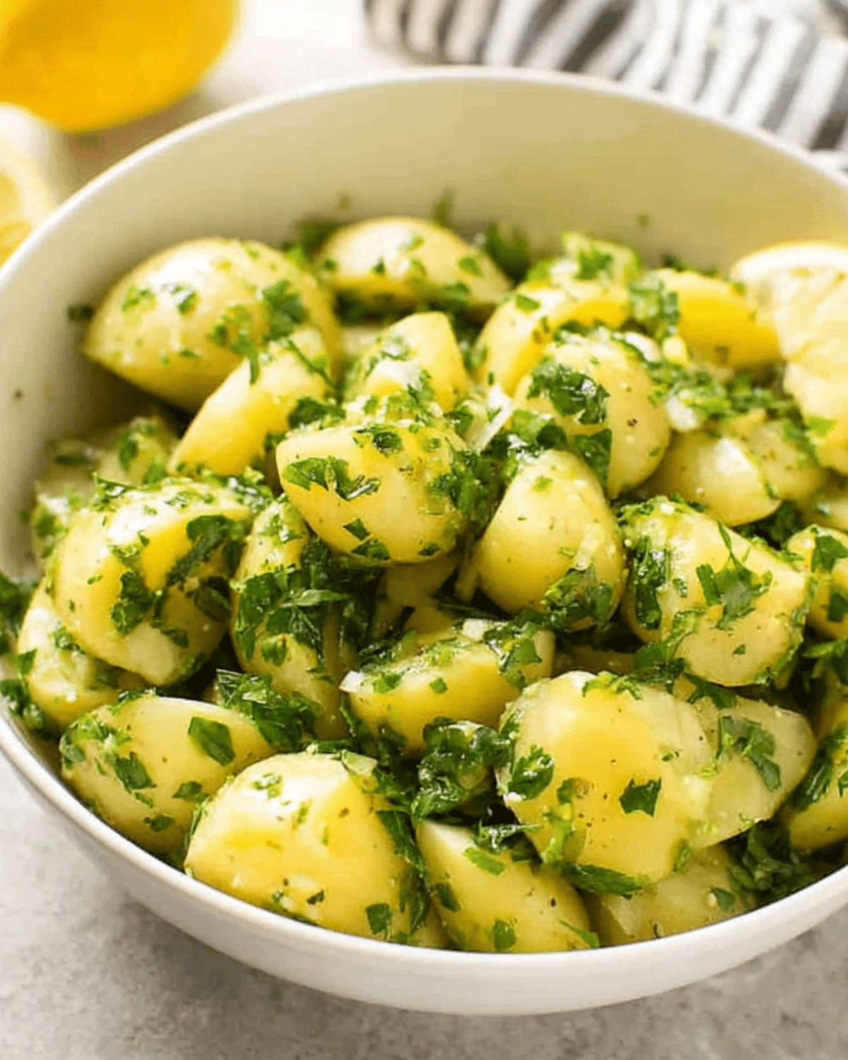 Lemon potato salad in a white bowl, featuring baby potatoes tossed with fresh herbs and a lemon vinaigrette.