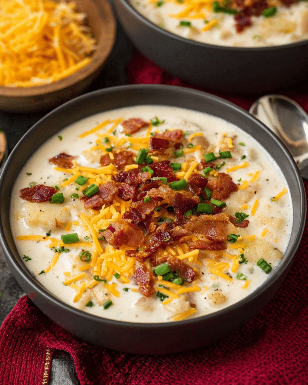A bowl of loaded baked potato soup topped with crispy bacon, shredded cheddar cheese, and chopped green onions.