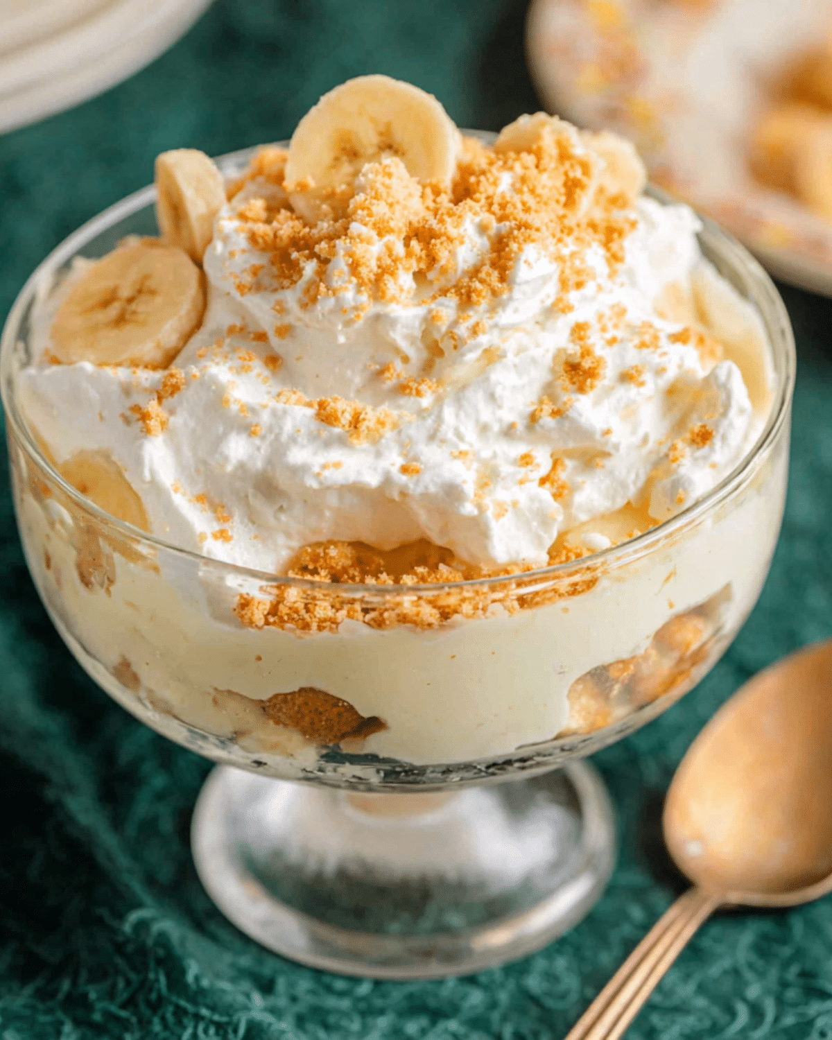 Glass dessert cup filled with layers of Magnolia Bakery banana pudding, sliced bananas, vanilla wafers, and topped with whipped cream and crushed cookie crumbs.