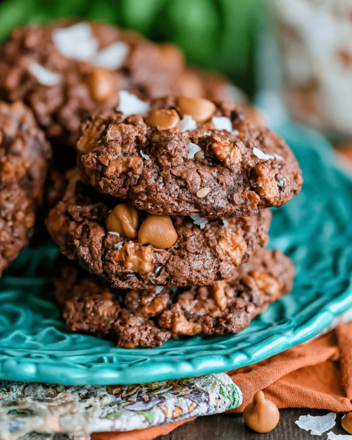 Stack of magic brownie cookies with gooey chocolate centers, butterscotch chips, and a sprinkle of flaky sea salt on a teal plate.
