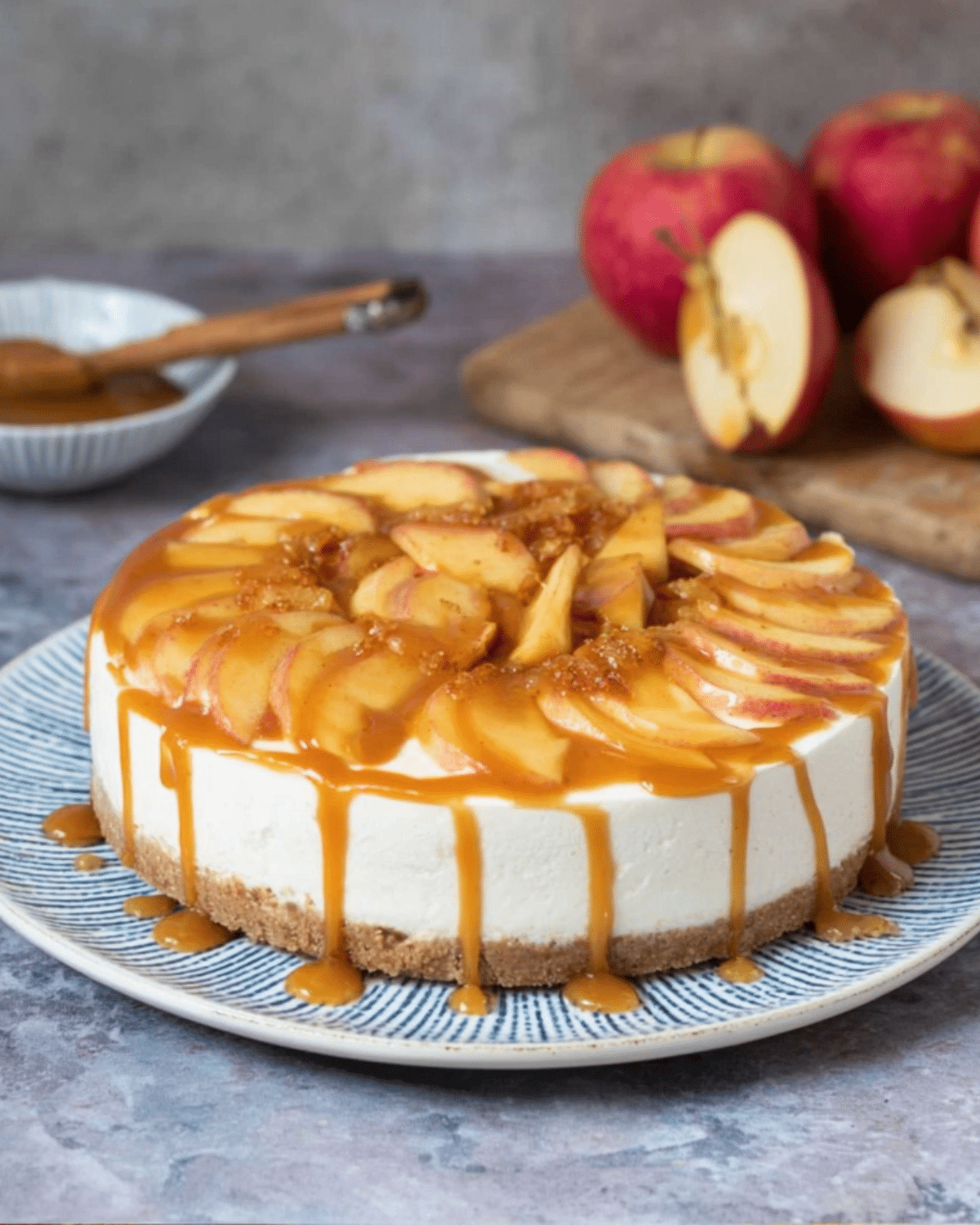 No Bake Apple Cheesecake topped with fresh apple slices and drizzled with caramel sauce on a patterned plate.