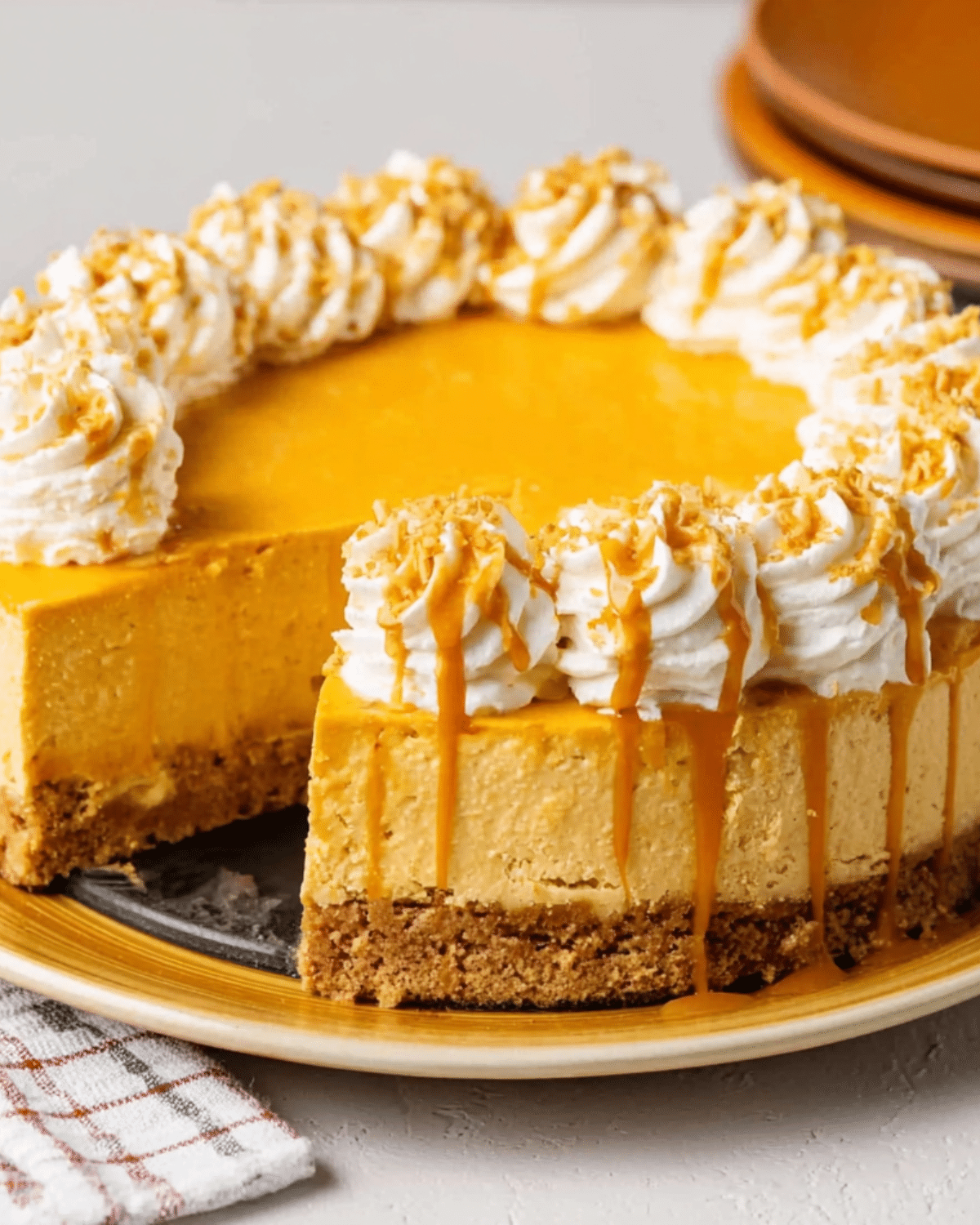 No Bake Pumpkin Cheesecake with a graham cracker crust, whipped cream swirls, and caramel drizzle on top.