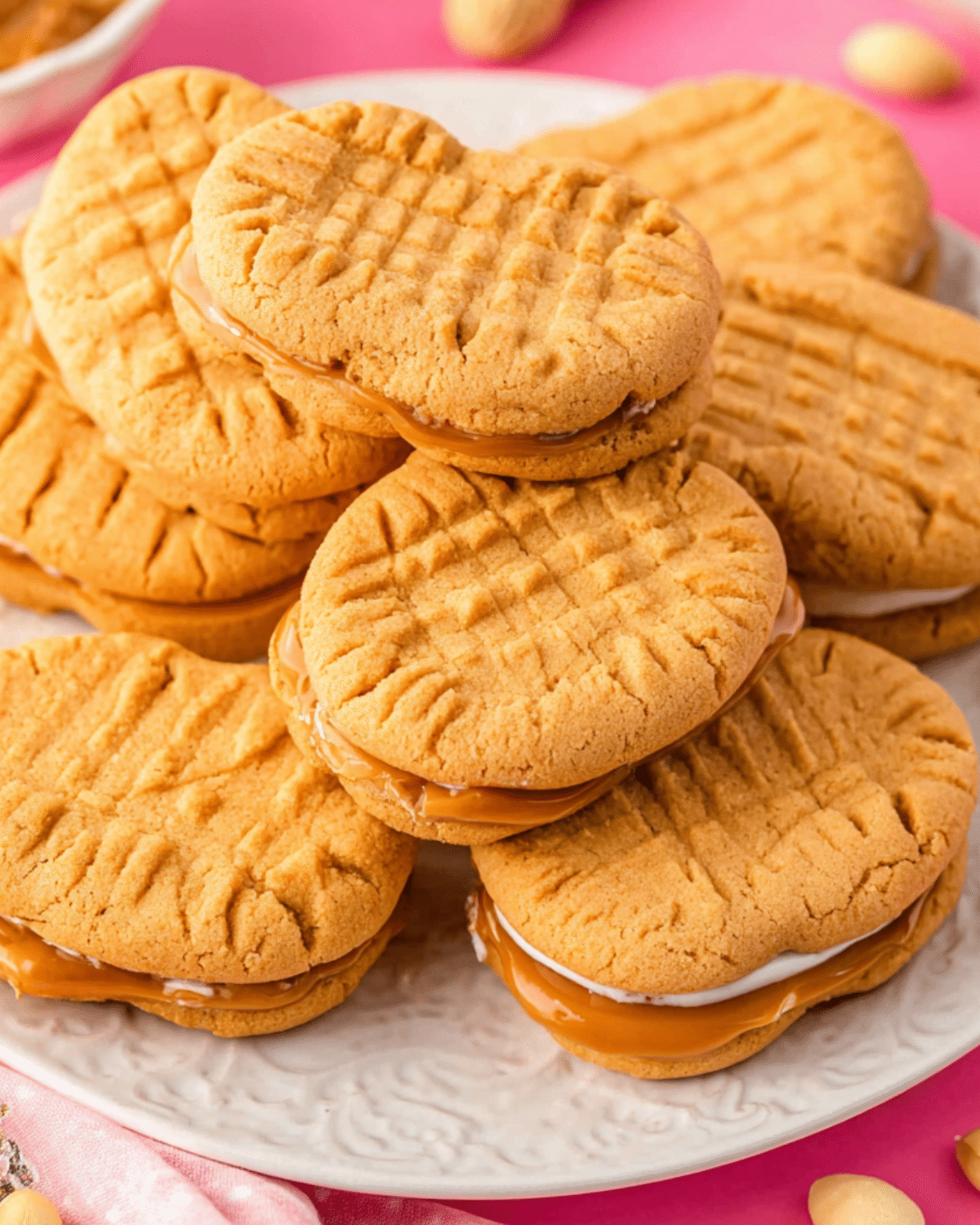 Homemade Nutter Butter cookies sandwiched with a creamy peanut butter and marshmallow filling, stacked on a white plate.