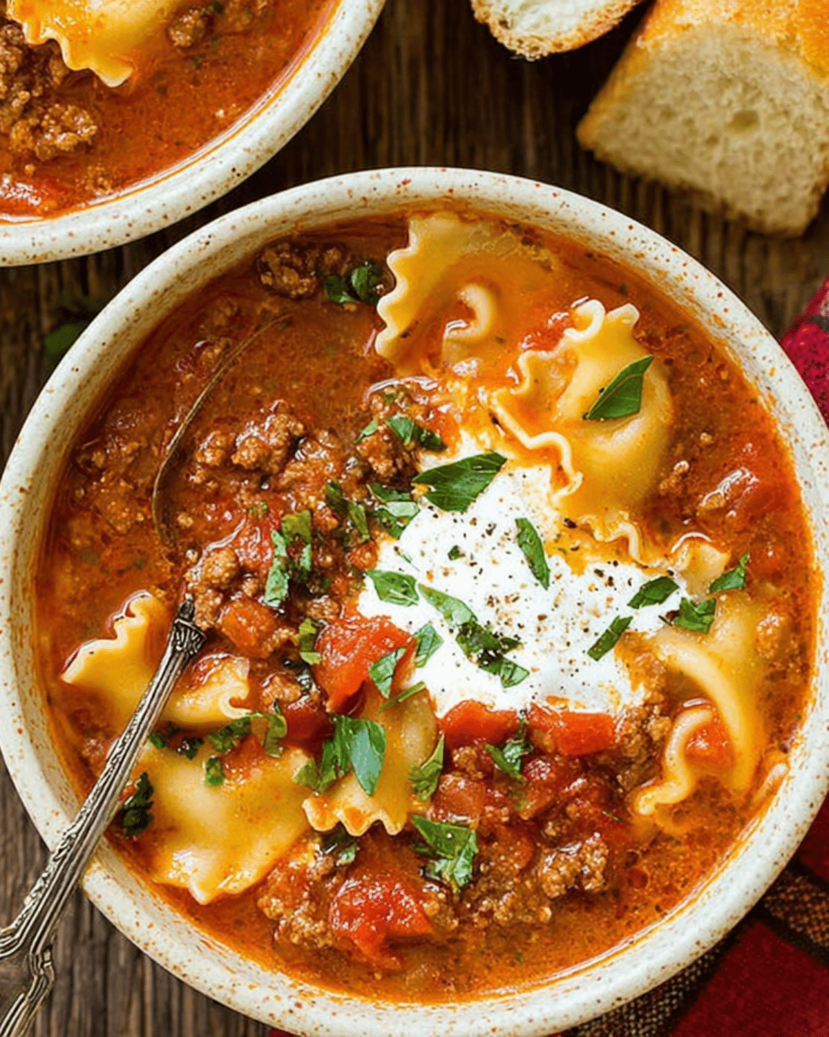 A hearty bowl of one-pot lasagna soup filled with ground meat, tomatoes, lasagna noodles, and topped with a dollop of ricotta and fresh herbs.